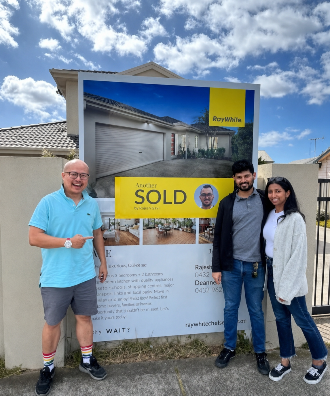 A man standing next to a smiling couple in front of a Ray White 'SOLD' real estate sign outside a house